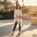 A woman smiling while wearing a flowing Beverly Hills tunic in a soft ivory color, paired with slim-fit dark jeans in a sunny outdoor setting.