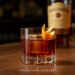 A perfectly crafted Bulleit Old Fashioned cocktail in a rocks glass, garnished with an orange peel and sitting next to a bottle of Bulleit Bourbon.