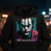 A person wearing a stylish black Joker hoodie with a vibrant graphic of the character's face on the front, standing against a blurred city background.