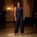 A woman smiling confidently while wearing a stylish navy blue lace jumpsuit at an evening event.