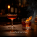 Manhattan cocktail in coupe glass next to Old Fashioned in rocks glass with orange peel garnish