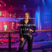 A stylish woman in a shimmering black sequin jumpsuit posing confidently inside a modern nightclub.
