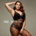 A smiling woman with curves wearing a stylish black lace plus size bodystocking, posing confidently against a neutral background.