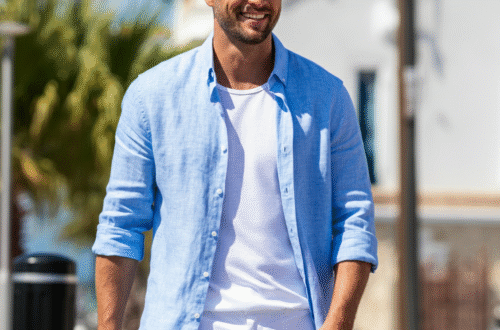 A stylish man wearing a light blue linen shirt and white chino shorts, smiling confidently on a sunny day.