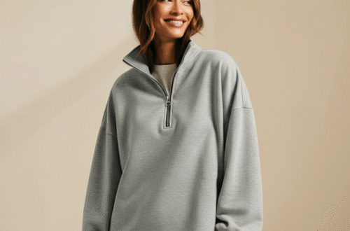 A stylish woman wearing a popular grey Trendy Queen oversized half-zip sweatshirt, smiling against a neutral background.