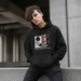 A stylish person wearing a black Pablo Escobar hoodie against a neutral urban background.