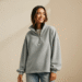 A stylish woman wearing a popular grey Trendy Queen oversized half-zip sweatshirt, smiling against a neutral background.
