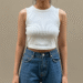 A person wearing a stylish white Von Dutch crop top with blue jeans, posing against a neutral background.