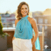 A woman wearing a stylish blue azura chiffon halter top, paired with white trousers and smiling in a bright, modern setting.