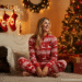 A happy family wearing matching red and white Christmas onesies while sitting in front of a decorated Christmas tree.