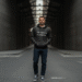 A person wearing a stylish black 'hennything is possible hoodie' paired with jeans, standing against a neutral urban background.