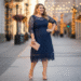 A woman wearing an elegant navy blue midi lace dress, smiling in a beautifully lit room.