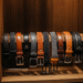 A collection of stylish leather belts for men hanging on a wooden rack, showcasing different colors and buckle styles.