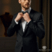 A man looking sharp and confident while adjusting the bow tie on his classic black mens tuxedo dinner suit.