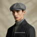 A man wearing a classic grey tweed newsboy cap, smiling slightly against a blurred urban background.