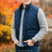 A person wearing a stylish navy blue quilted vest over a gray sweater, standing outdoors on a crisp autumn day.